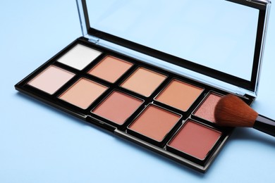Photo of Contouring palette and brush on light blue background. Professional cosmetic product