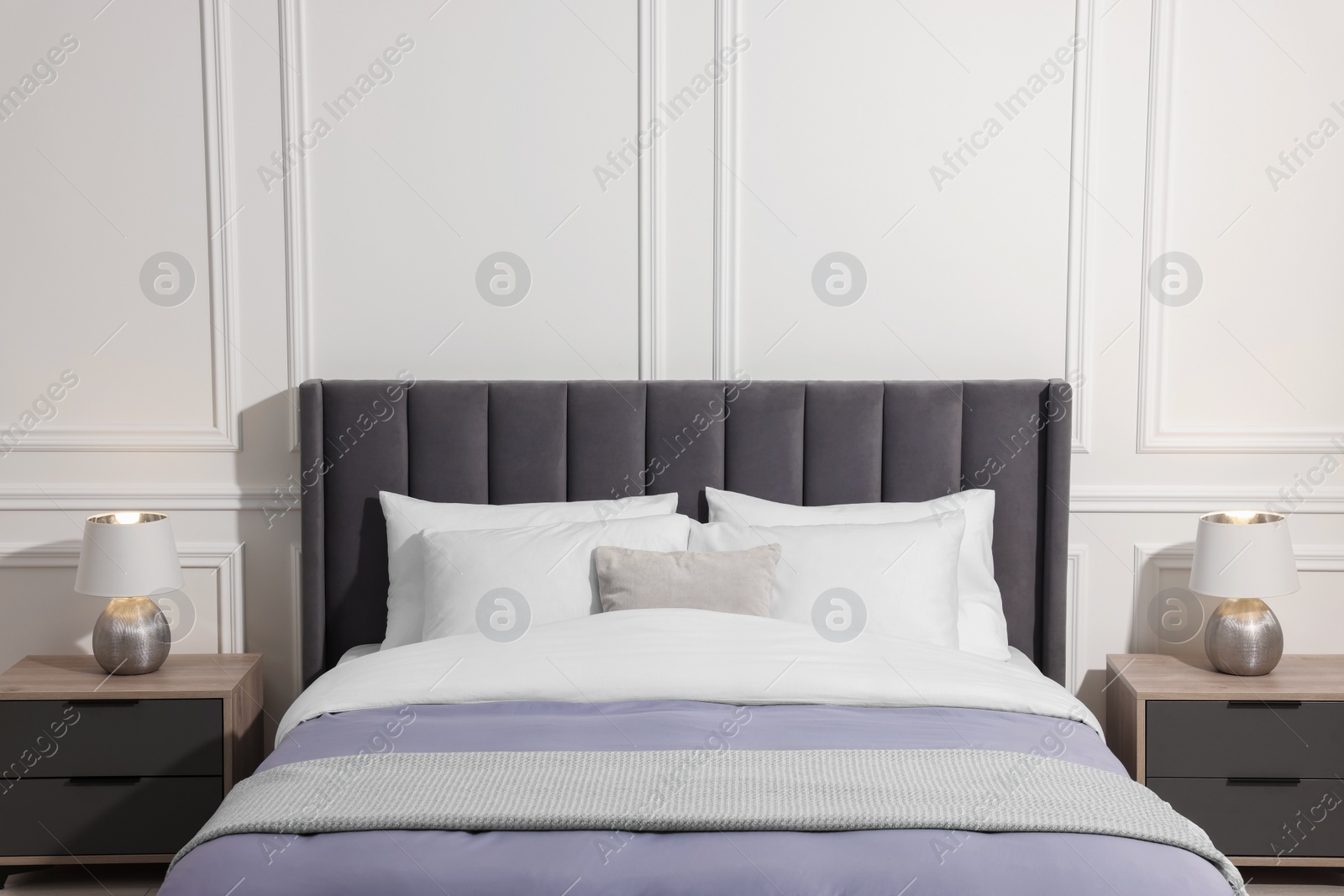 Photo of Comfortable bed between bedside tables with lamps at home. Interior design