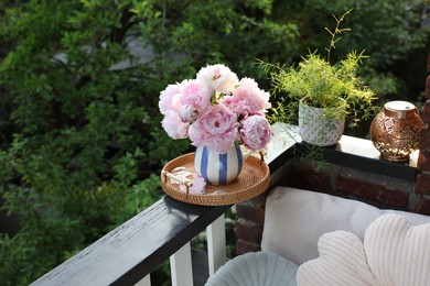 Beautiful pink peony flowers in vase and potted plant on balcony railing outdoors