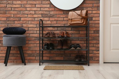 Photo of Rack with different shoes near red brick wall in hallway