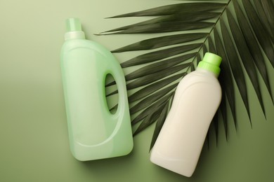 Photo of Bottles of fabric softener and palm leaf on light green background, flat lay