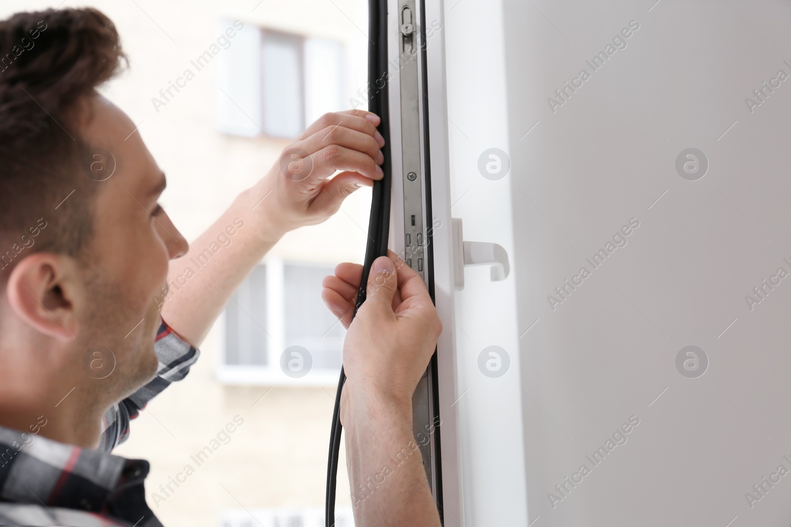 Photo of Young man putting sealing foam tape on window indoors