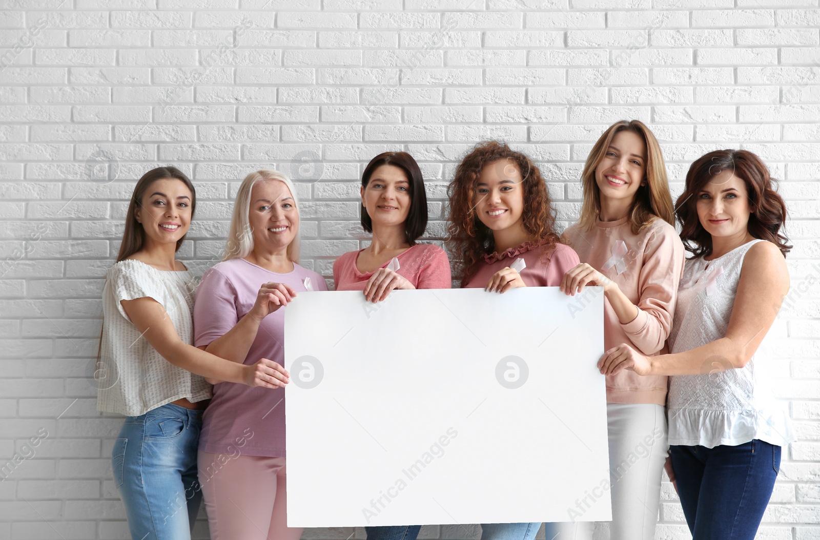 Photo of Women wearing silk ribbons holding poster with space for text against brick wall. Breast cancer awareness concept