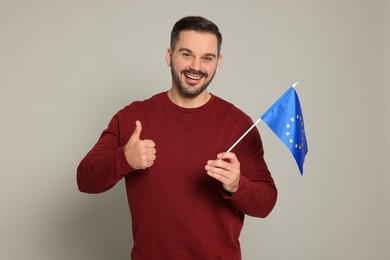 Photo of Man with flag of European Union showing thumb up on light grey background