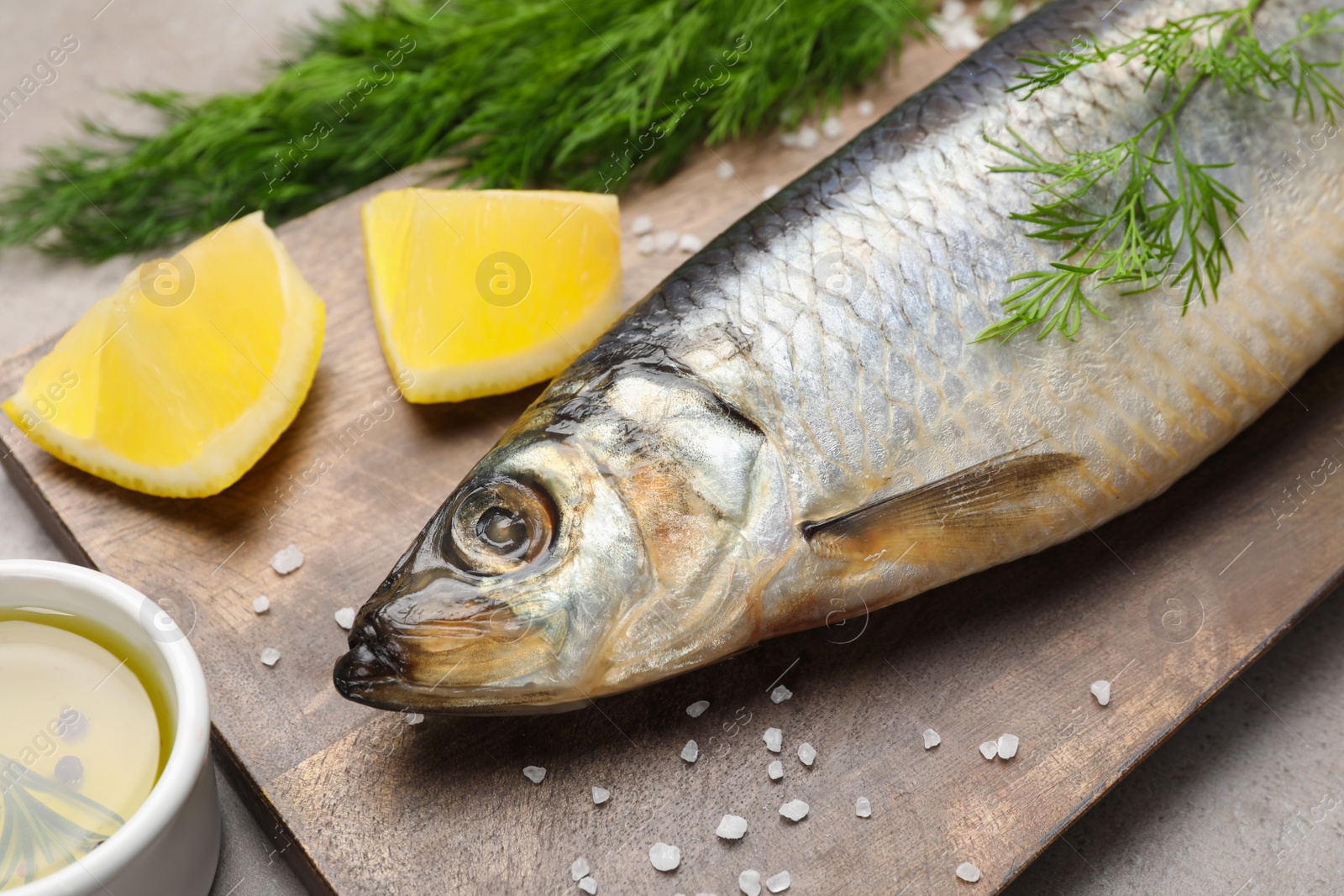 Photo of Board with delicious salted herring, dill, lemon and olive oil on grey table, closeup