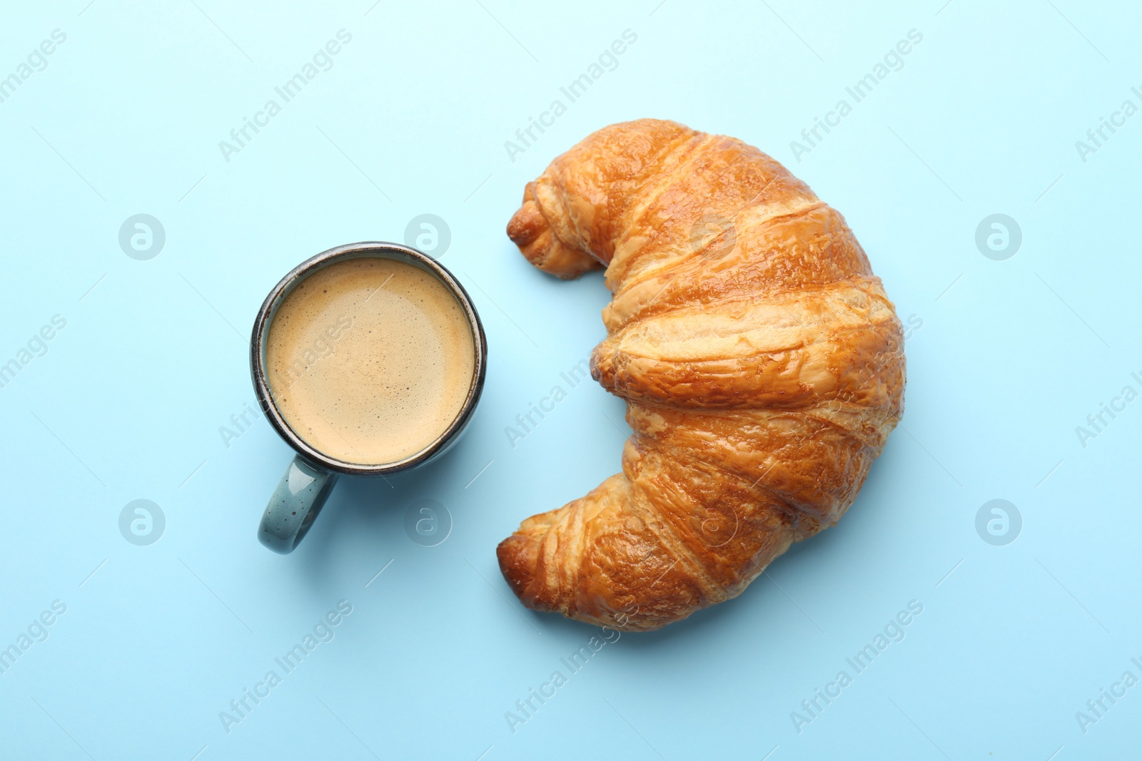 Photo of Delicious fresh croissant and cup of coffee on light blue background, flat lay