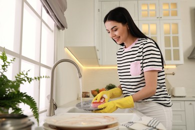 Photo of Woman washing plate above sink in kitchen