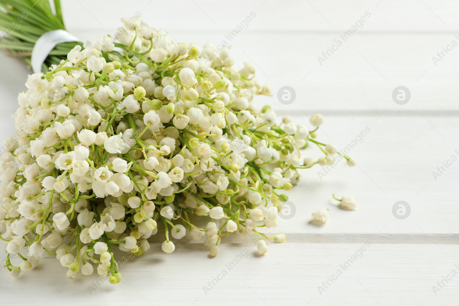 Photo of Beautiful lily of the valley bouquet on white wooden table, closeup. Space for text