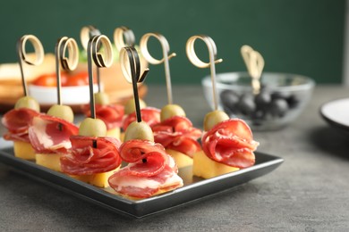 Photo of Tasty canapes with olives, prosciutto and cheese on grey table, closeup