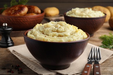 Photo of Bowl of tasty mashed potatoes with black pepper served on wooden table