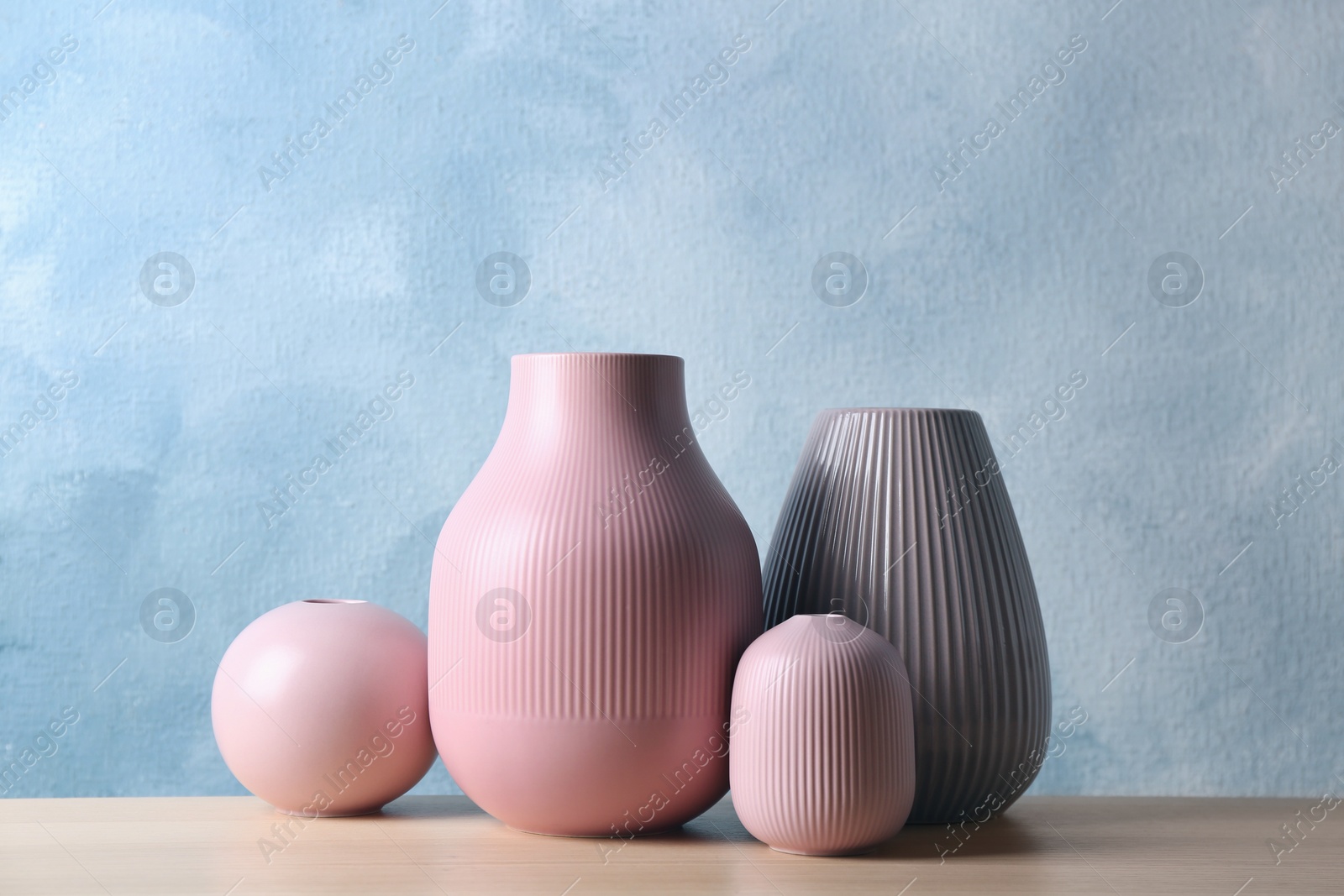 Photo of Stylish ceramic vases on wooden table against light blue background