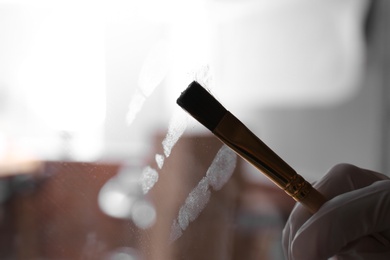 Photo of Detective using brush and powder to reveal fingerprints on glass surface indoors, closeup