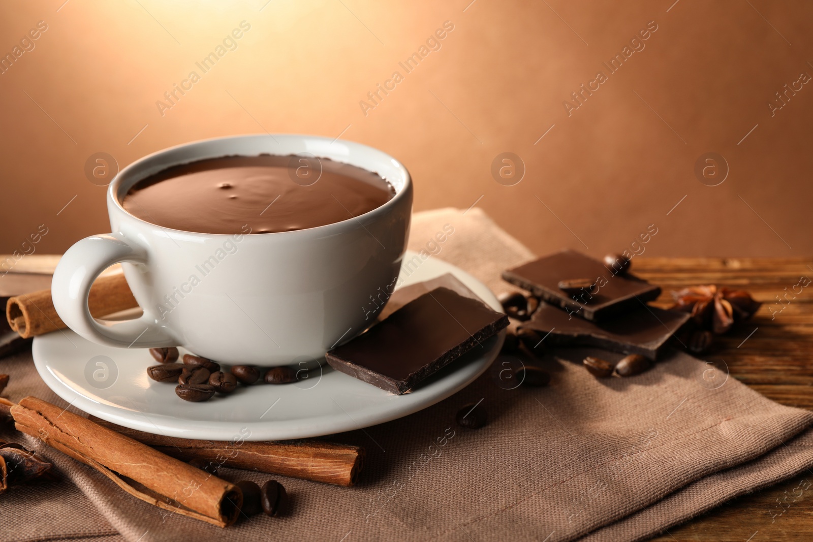 Photo of Cup of delicious hot chocolate, spices and coffee beans on wooden table. Space for text