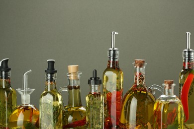 Photo of Cooking oil with different spices and herbs in bottles on grey background