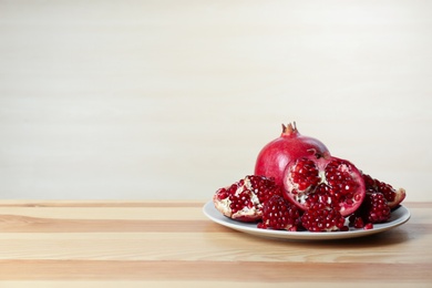 Plate with ripe pomegranates on table against light background, space for text