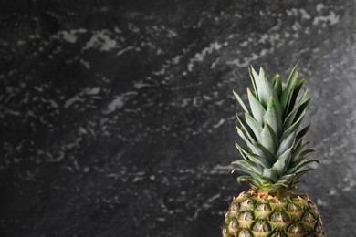 Photo of Whole ripe pineapple near black wall, closeup. Space for text