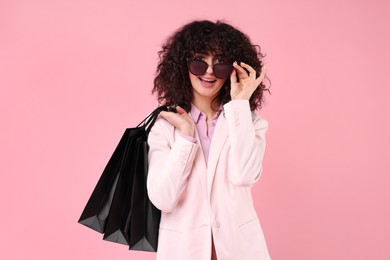 Photo of Happy young woman with shopping bags and stylish sunglasses on pink background