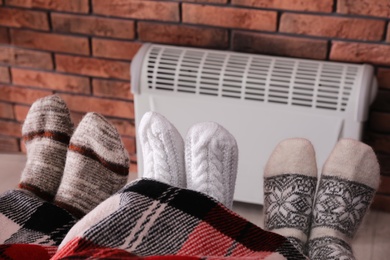 Photo of Family warming feet near electric heater at home, closeup