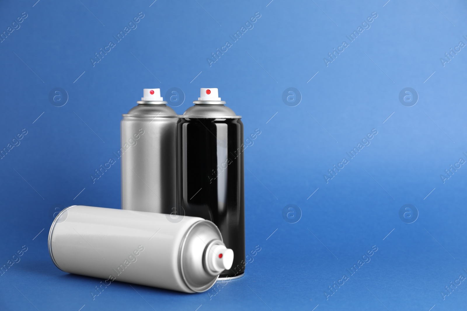 Photo of Cans of spray paint on blue background. Space for text