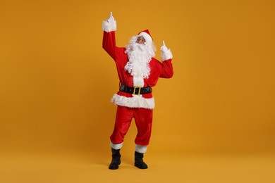 Photo of Merry Christmas. Santa Claus pointing at something on orange background