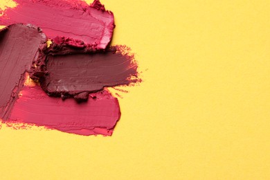 Photo of Smears of bright lipsticks on yellow background, top view. Space for text
