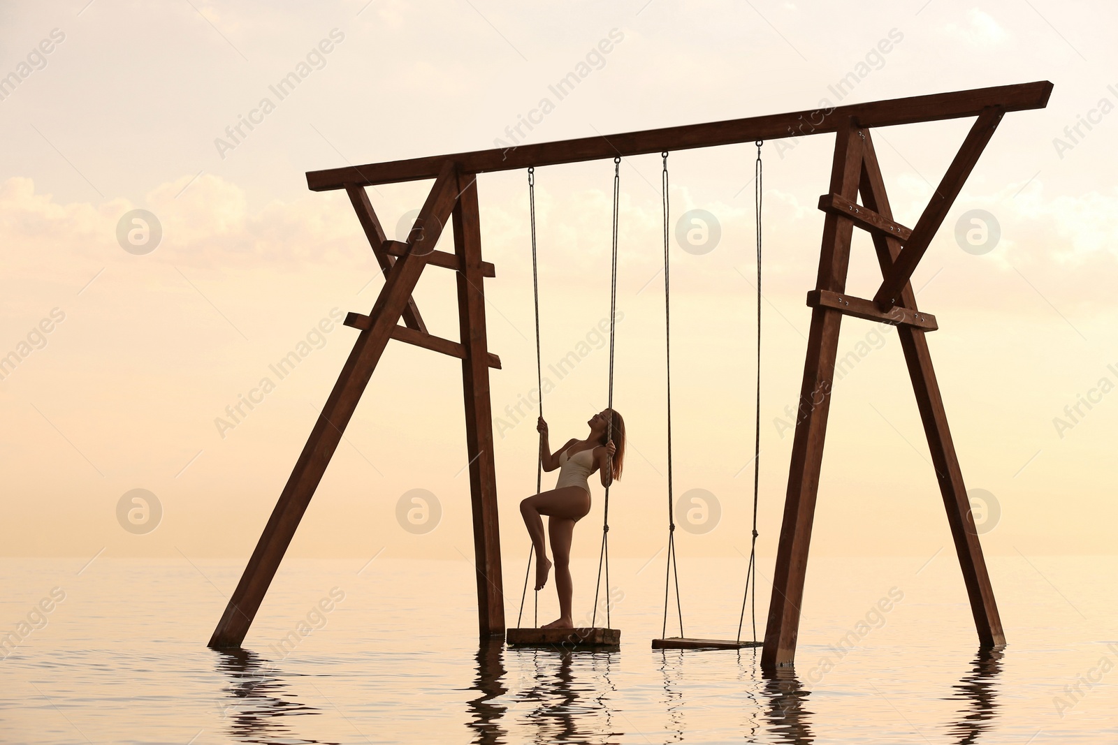 Photo of Young woman enjoying sunrise on swing over water