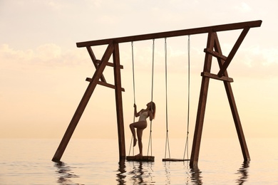 Young woman enjoying sunrise on swing over water