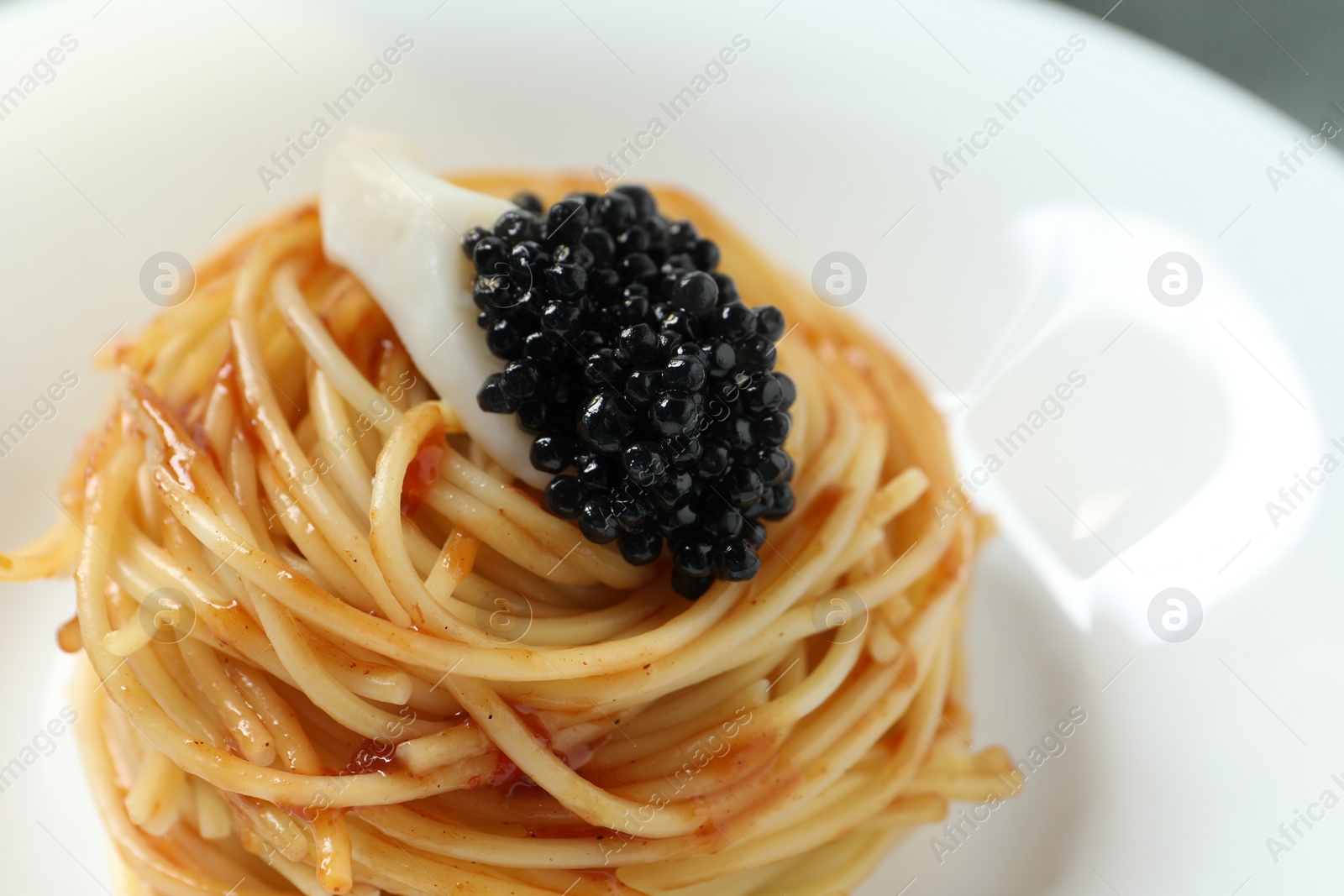 Photo of Tasty spaghetti with tomato sauce and black caviar on plate, closeup. Exquisite presentation of pasta dish