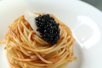 Tasty spaghetti with tomato sauce and black caviar on plate, closeup. Exquisite presentation of pasta dish