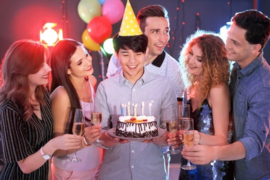 Photo of Young people celebrating birthday with cake in nightclub
