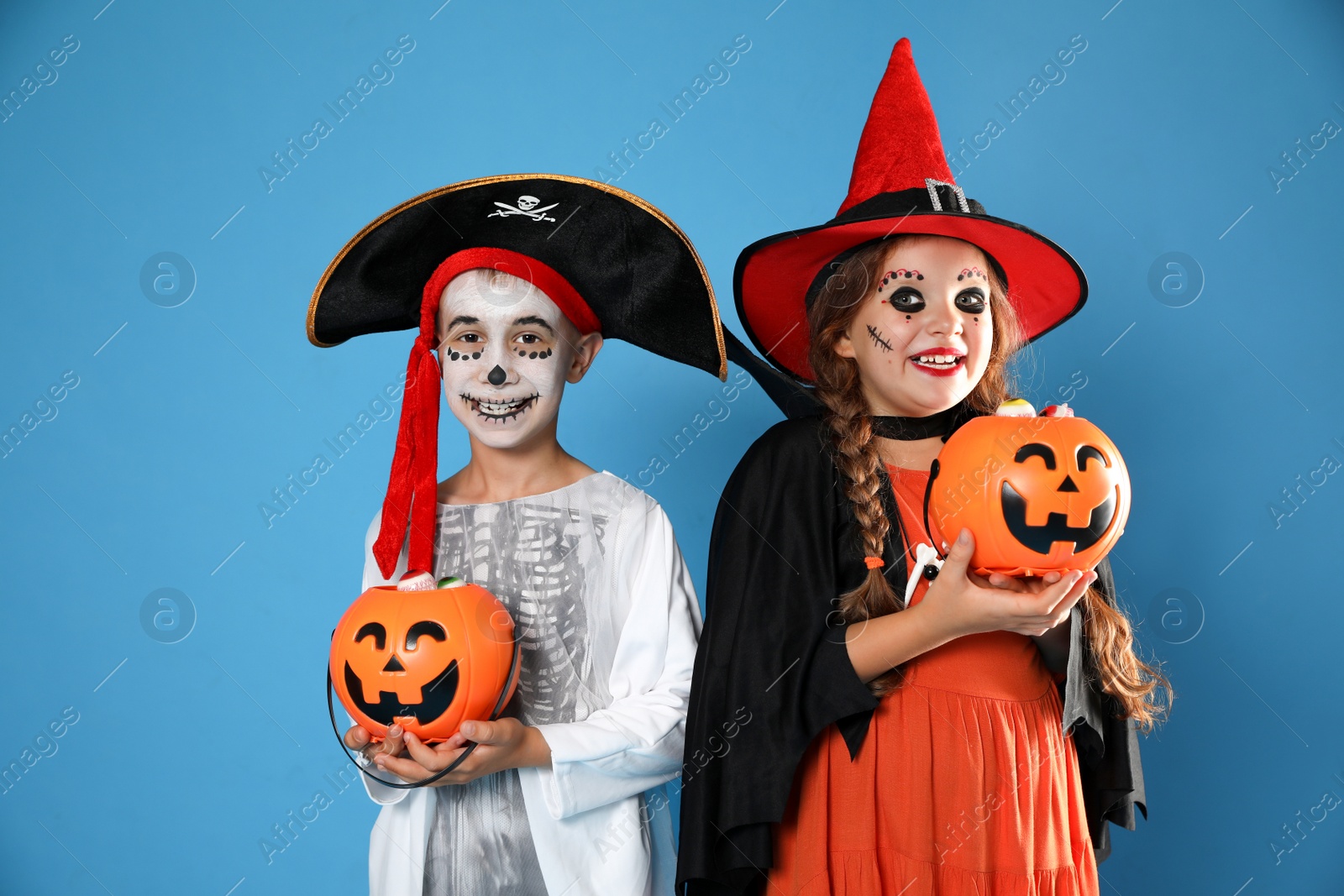 Photo of Cute little kids with pumpkin candy buckets wearing Halloween costumes on blue background