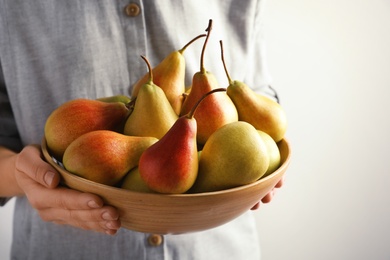 Photo of Woman holding bowl with ripe pears on light background, closeup