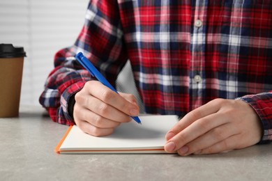 Photo of Woman with pen and notepad at grey table, closeup