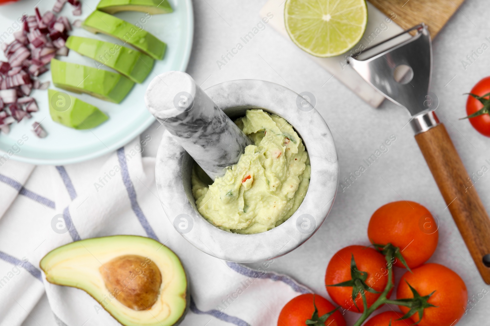 Photo of Mortar with delicious guacamole and ingredients on white table, flat lay