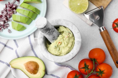 Mortar with delicious guacamole and ingredients on white table, flat lay