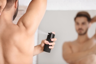 Handsome young man applying deodorant in room. Space for text