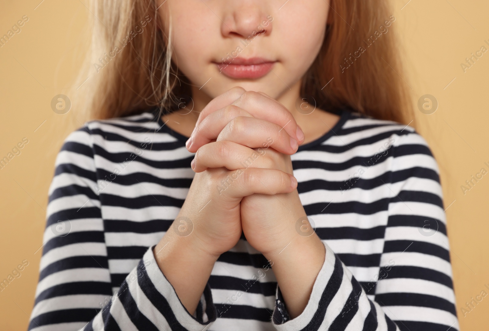 Photo of Girl with clasped hands praying on beige background, closeup
