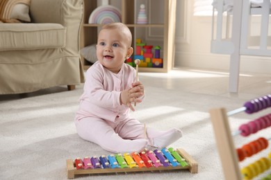 Photo of Cute baby girl playing with xylophone on floor at home