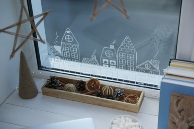 Photo of Christmas decor on white wooden table near window with beautiful drawing at home