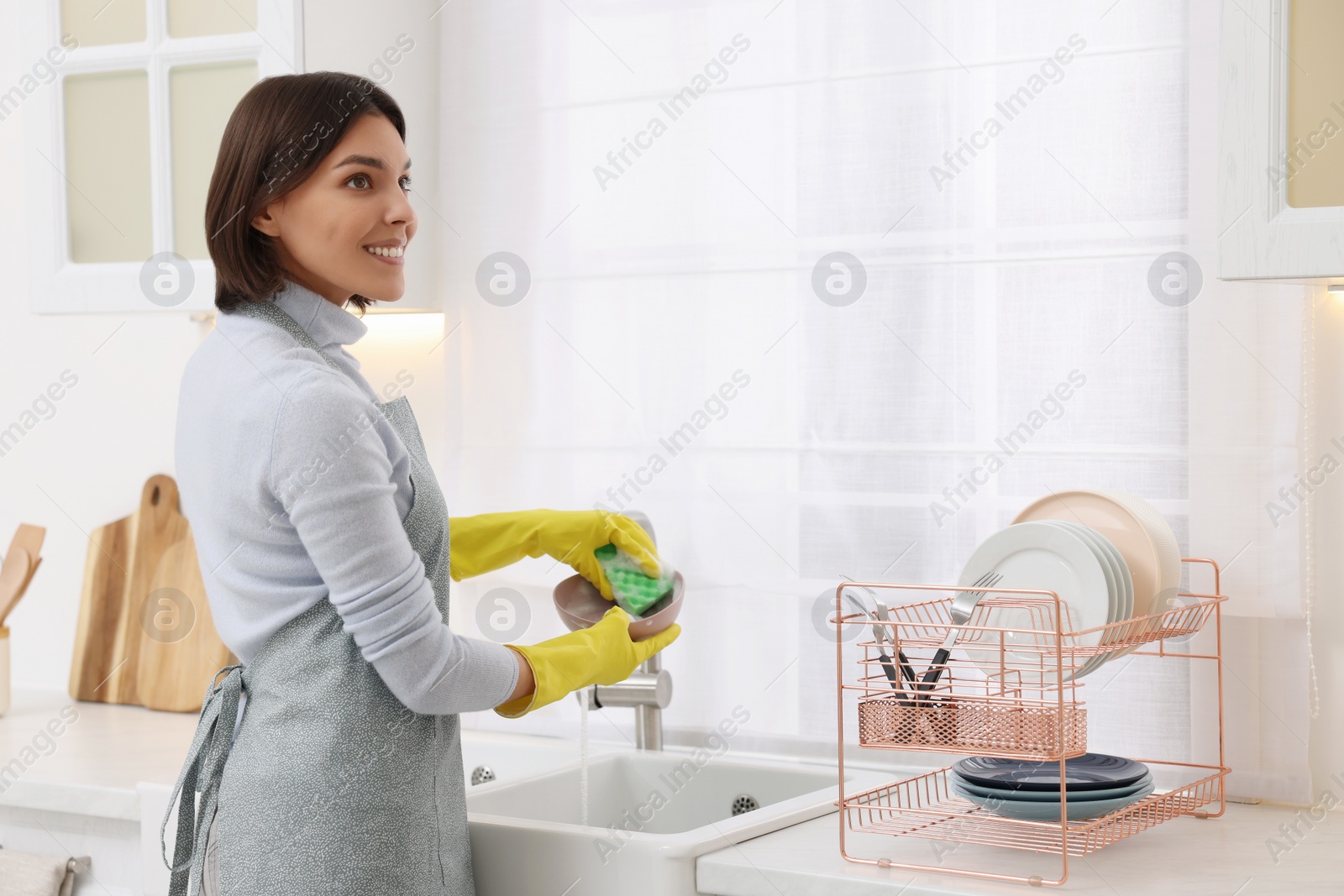 Photo of Happy young woman washing plate above sink in modern kitchen