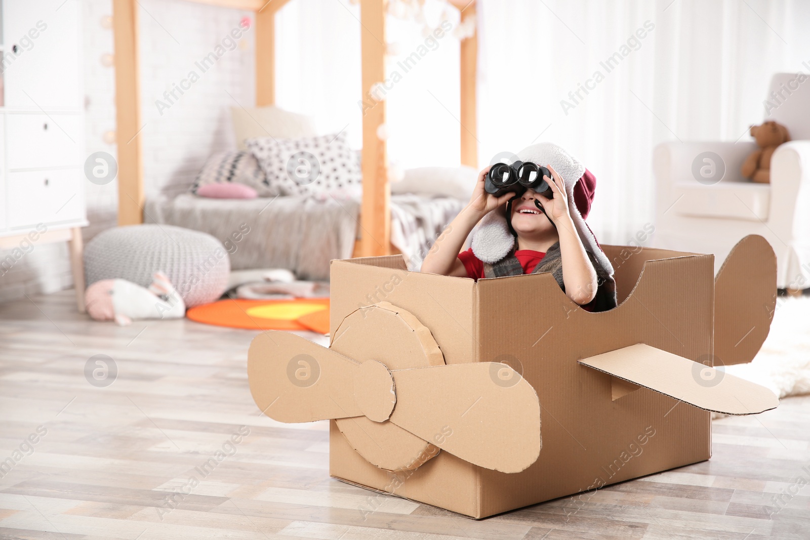 Photo of Cute little boy playing with binoculars and cardboard airplane in bedroom