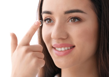 Young woman putting contact lens in her eye on light background