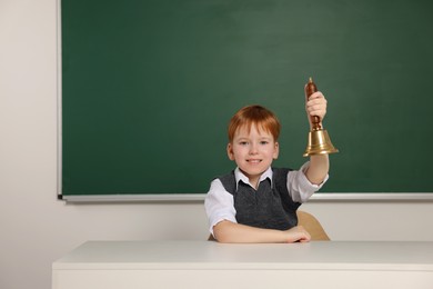Photo of Cute little boy ringing school bell in classroom, space for text