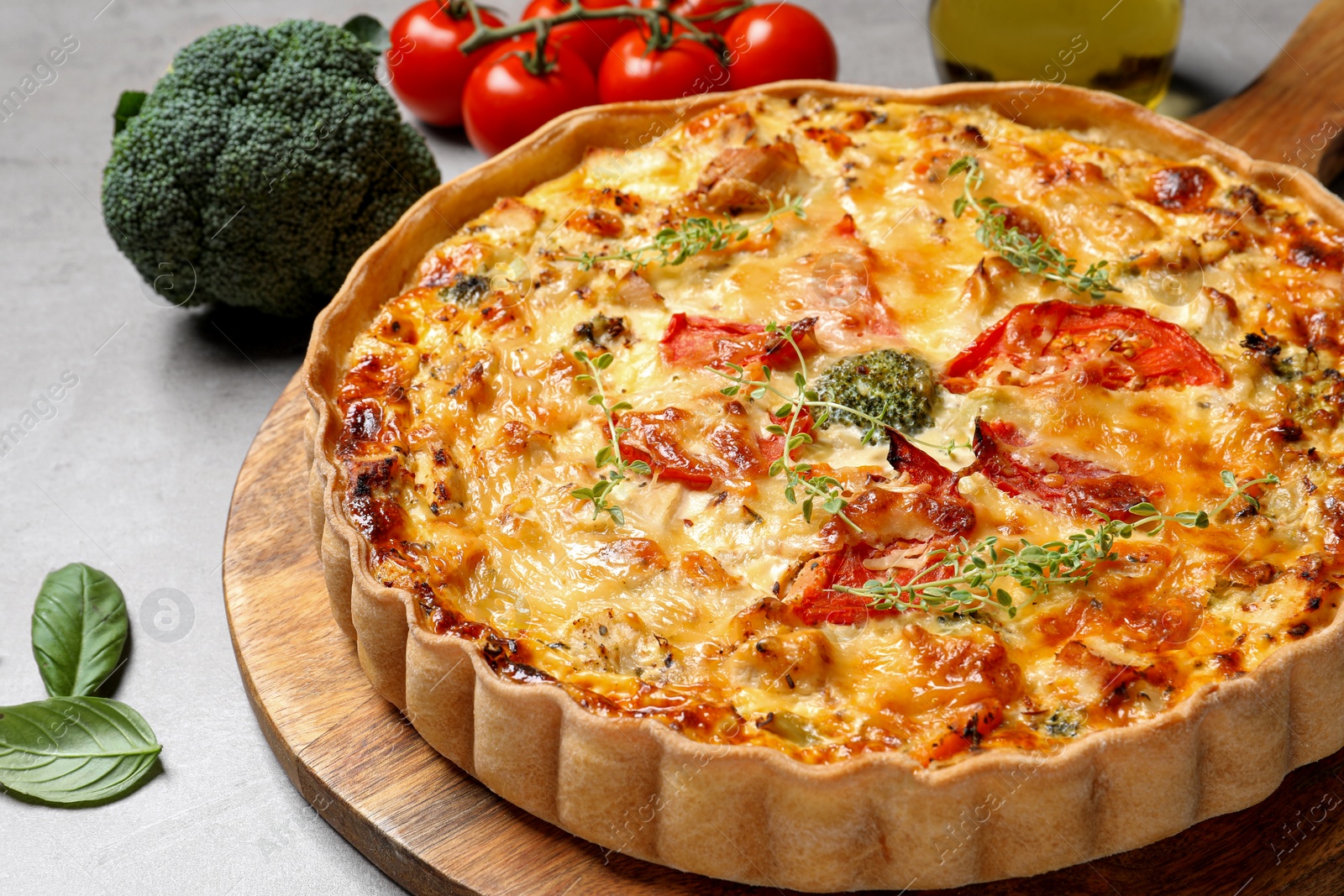 Photo of Tasty cheese quiche and ingredients on light grey table, closeup