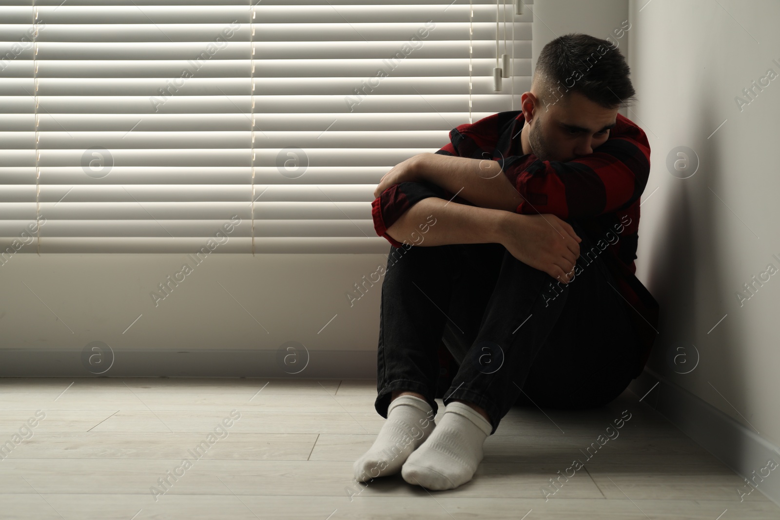 Photo of Sad man sitting on floor at home. Space for text