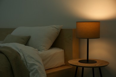 Photo of Stylish lamp on table near bed indoors