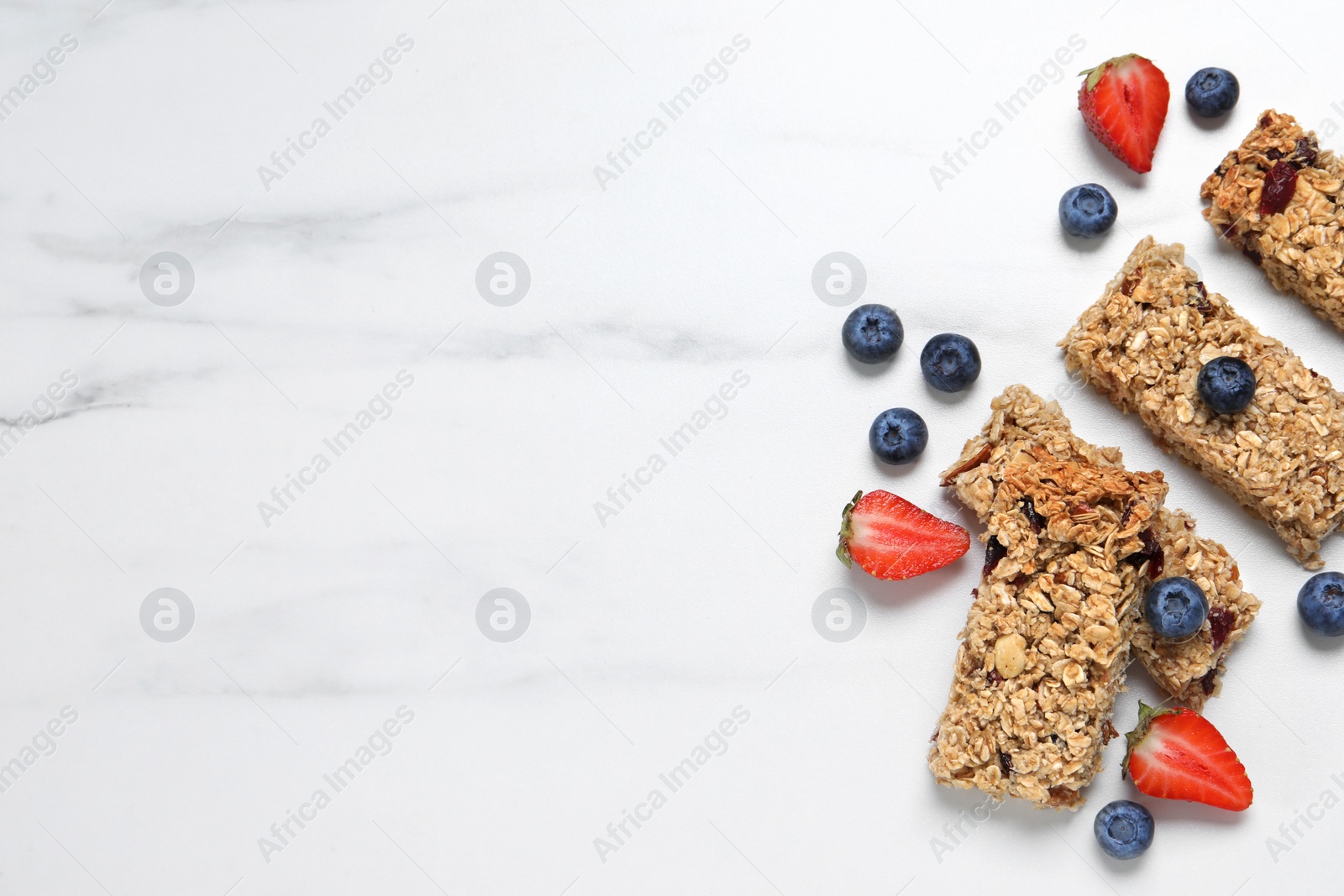 Photo of Tasty granola bars and berries on white marble table, flat lay. Space for text