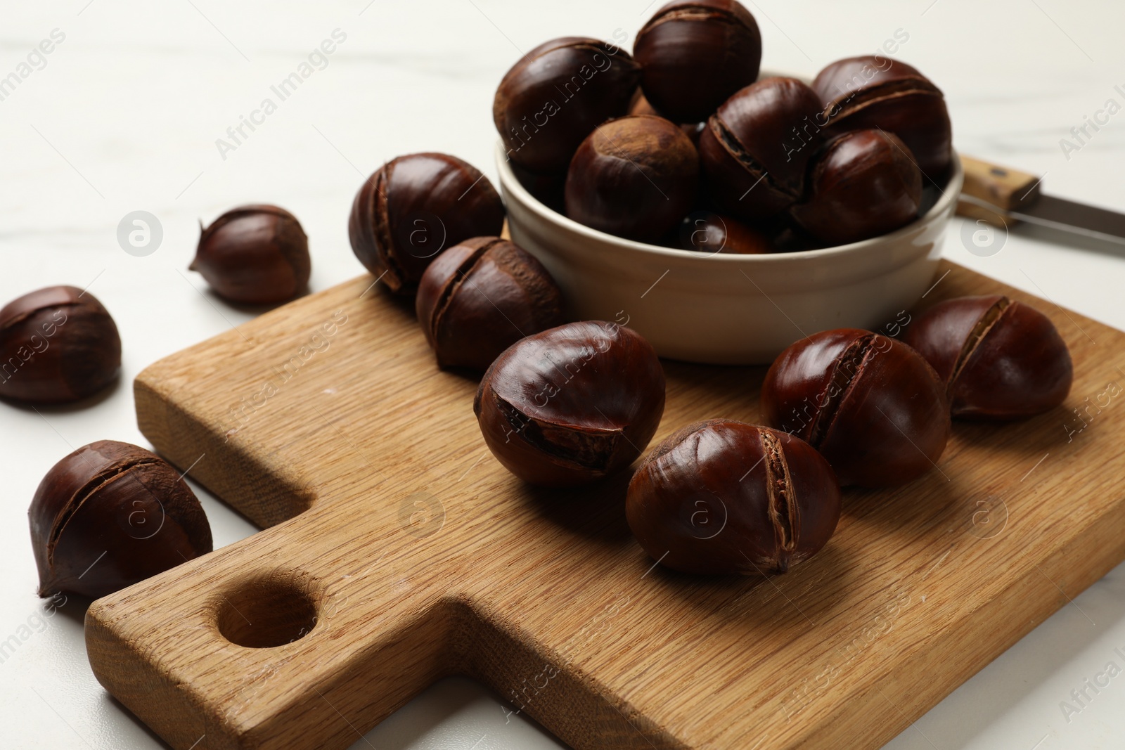 Photo of Bowl with roasted edible sweet chestnuts on white table, closeup