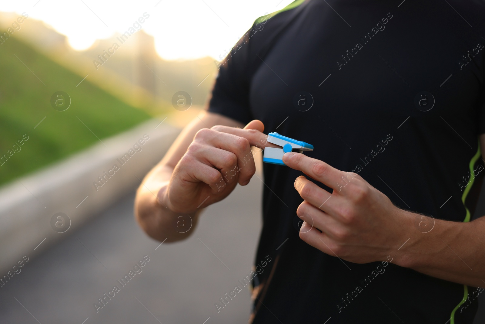 Photo of Man checking pulse with blood pressure monitor on finger after training in park, closeup. Space for text