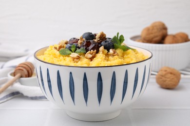 Photo of Tasty cornmeal with blueberries, dates, walnuts and mint in bowl on white table, closeup